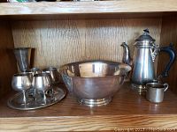 Wide view of shelf with large bowl, teapot, small cup, and group of goblets on a round tray
