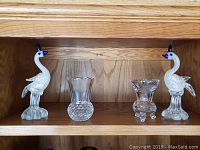 Two glass bird figurines flanking a clear textured glass candle holder on wooden shelf.