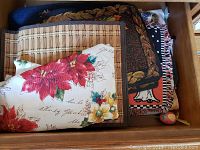 Drawer showing folded tablecloth with poinsettia design, woven autumn-themed runner, and other folded linens