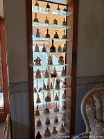 Full-height glass shelving unit displaying multiple rows of assorted decorative bells.