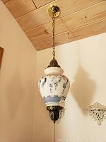 Full photo of a hanging lamp with white glass body, decorated with blue hand painted floral patterns, brass chain and fittings.