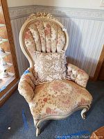 Front view of one chair with carved floral crest, tufted back, scrolled arms and decorative pillow on seat.