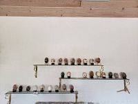 Wide shot showing all 27 egg shaped decorative pieces arranged on three glass shelves with gold brackets, varying colors and stands.