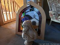 The ceramic figurine bust in front of the stained glass panel, showing scale and design.