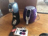 Photo of black SodaStream carbonator and purple GoWISE USA air fryer on wood table surface along with instruction manuals.