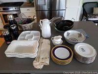 Full lot displayed on kitchen counter including plates, fruit bowl, woks, thermoses, napkins, pitcher, and serving dishes