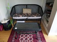 Photo showing full loveseat with two floral cushions and matching rattan coffee table on a red patterned rug.
