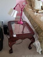 Full view of side table with glass inset and lamp on top placed beside the bed