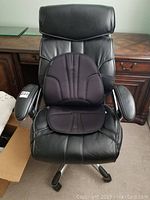 Front view of black leather office chair with Homedics black seat pad placed on the seat, showing armrests and headrest