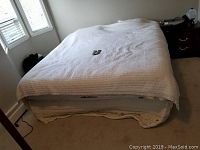 Full view of the Sleep Number electric adjustable bed with white cover and beige carpet beneath.