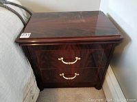 Front view of night table showing two drawers with brass handles and high gloss wood surface with inlay design.