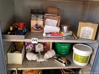 Shelf with assorted bath hardware, lighting, and small tools including spotlight fixture, timer, sanding kit, caulking gun, spool of wire, and container of gel.