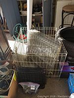 Photo showing metal wire pet cage panels arranged inside and around the cage base with black shelving unit panels in front.