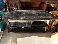 Front view of the TV stand showing three black tinted glass shelves held by curved dark wood legs.