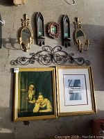 Full lot showing framed art pieces, wall sconces, small carved frame, and metal wall swag arranged on ground.