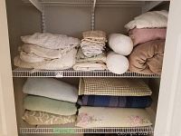 Photo of upper and middle shelving with various folded bedding including sheets, cushions, and blankets.
