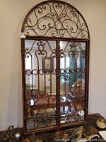 Full front view of the wall mirror with two metal framed mirrored doors and arched top.