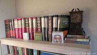 Top shelf of bookshelf with Bibles, religious books, a small desk calendar, and vintage-style wooden clock.