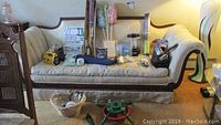 Full view of many home goods on an old beige couch, including radio, cleaning supplies, and hardware items on and in front of couch.