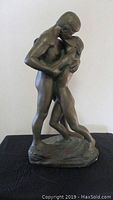 Front view of the bronze-finished sculpture showing two nude lovers embracing on a textured base.