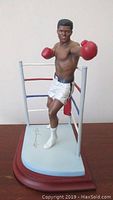 Front angled view of Muhammad Ali sculpture in boxing stance on blue base with ring ropes