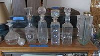 Six glass decanters including round, square and rectangular shapes with stoppers on a wooden surface