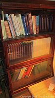 Books arranged on a wooden bookshelf: several hardcover titles including encyclopedias and assorted topics.