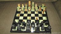 Chess board with all pieces set up on board, showing alternating black and marble colored squares, chess pieces in black and light green beige marble, some visible chips on pieces.