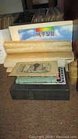 Photo of vintage books and manuals stacked on the floor including 'Adventures of Tom Sawyer' and some rolled posters/calendars with visible Korean calendar on top.