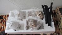 Four solar owl garden lights nestled in white foam packaging, each wrapped in plastic, with metal stakes attached.