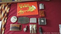 Photo showing the collection of Esso collectibles including the miniature tool kit shaped like a tire, Esso tire key chain, Bet Your Boots booklet, lighters, pins, and different belt buckles laid on a maroon cloth.