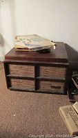 Photo of vintage wooden cabinet housing the record player and sheet music on top, showing overall condition and wear.