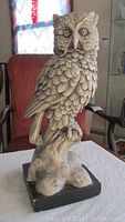 Front view of a detailed ceramic owl sculpture showing textured feathers, large eyes, pointed beak, perched on a root-like base painted black.