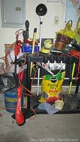 A photo of a collection of garden and yard tools including a black plastic tool stand with slots and gardening containers like pots and bags of soil mix and gloves.