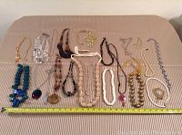 Full view of 22 necklaces laid out on a beige surface with a ruler showing length