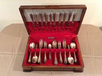 Full view of cutlery set inside wooden chest with red lining. Shows arrangement of knives, forks, and spoons.
