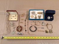 Photo showing assorted jewelry laid out including necklaces, bracelets, brooches, earrings, rings, buttons, and cufflinks. Various styles and sizes.