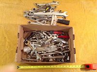 Overview of loose wrenches and sockets in a cardboard box showing a variety of mechanics tools in used condition.