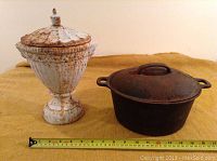 Both items placed on a yellow cloth; shows the bean pot and white urn side by side with a measuring tape in front for size reference.