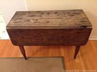 Front view of antique drop leaf table with both leaves down, showing worn wooden surface and visible age wear.