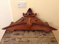 Front view of the entire carved wood piece showing its triangular shape and detailed adornments.