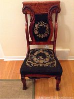 Front view of antique claw foot parlour chair showing needlepoint floral upholstery on seat and backrest, carved wood frame with armrests.