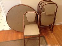 Full set including 36-inch round folding card table and four matching beige padded metal folding chairs.