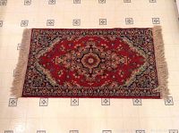 Full view of the rectangular oriental rug on a tiled floor, showing fringed edges and vibrant red and navy design.
