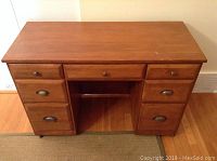 Full front view of the wooden desk or vanity dresser showing 7 drawers and metal hardware.