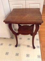 Full view of the antique parlour table showing four curved legs, lower shelf, and wooden top with wear.