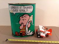Green metal garbage can with Peanuts Linus image and quote, showing wear and rust inside.