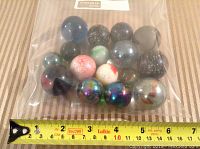 Plastic bag containing 16 assorted glass marbles, mostly larger around 1.25 inches with variety of colors and patterns, with ruler for size reference.