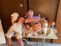 Full view of all dolls and stuffed toys on table including Raggedy Ann, various dolls, and stuffed poodles