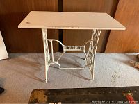 Front view of the vintage Singer sewing table, showing the rectangular particle board top and ornate white cast iron base with Singer logo.